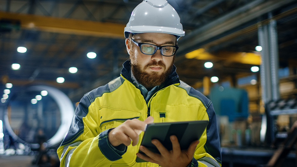 Factory worker wearing a hardhat and high vis clothing, using a tablet